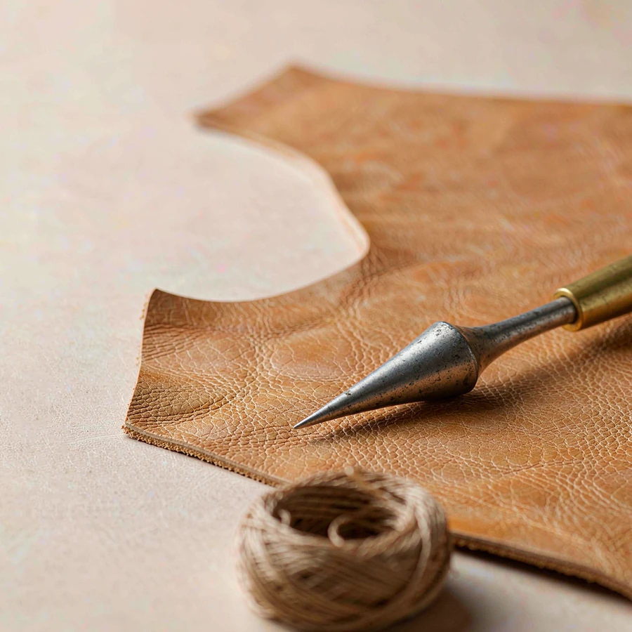 Full-grain tan leather with a brass awl and a coil of waxed thread