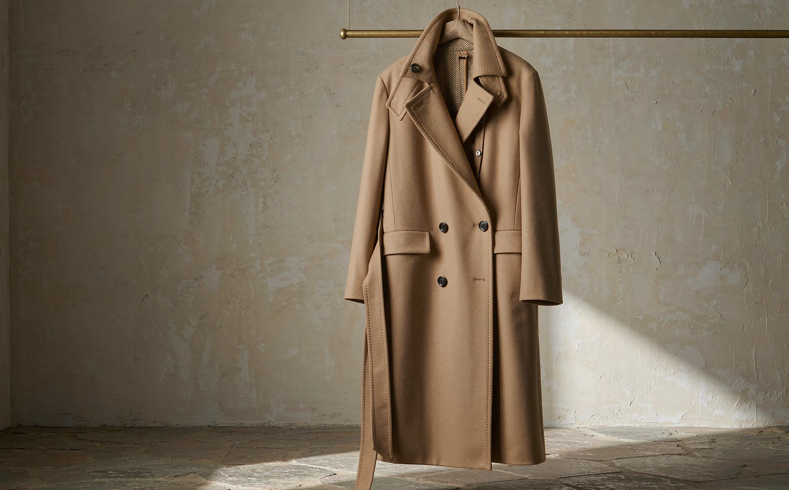 Camel wool and cashmere coat on a brass rail in a sunlit atelier